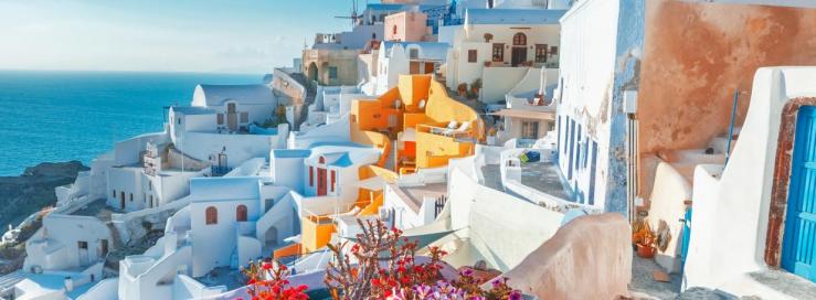 Santorini, Greece. Picturesq view of traditional cycladic Santorini houses on small street with flowers in foreground. Location - Oia village, Santorini, Greece. Vacations background_hero@1950x455